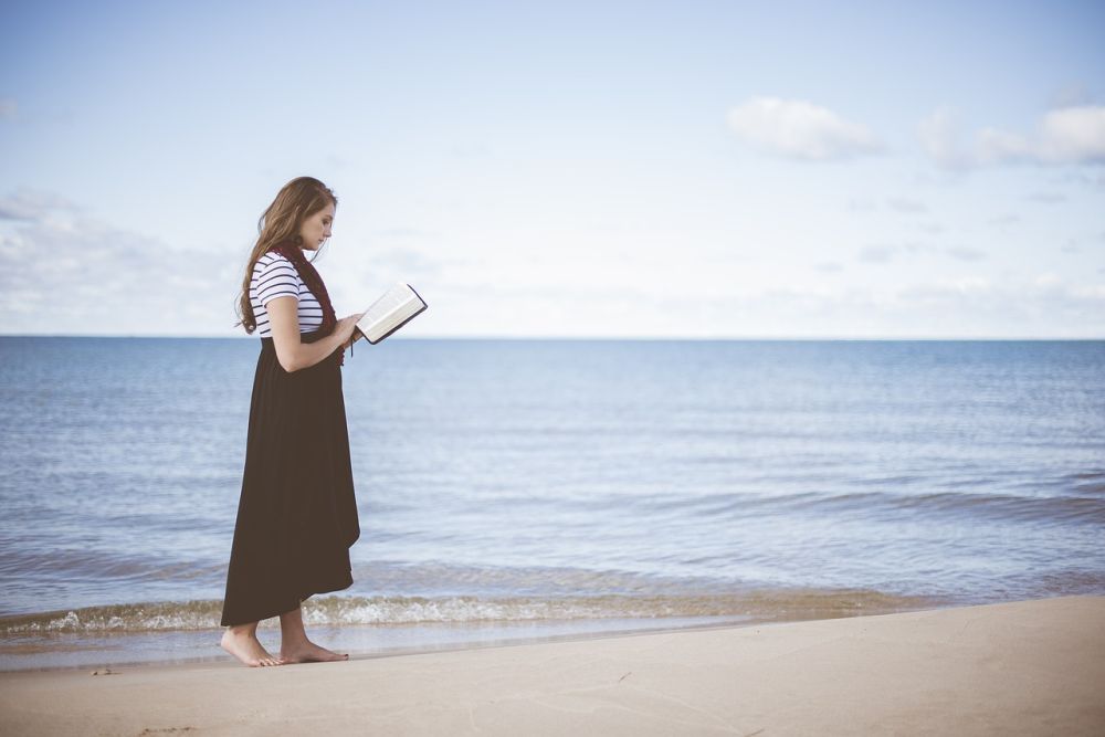 Žena stojí a číta knihu pri mori